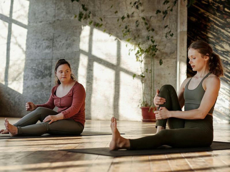 A person in a deep stretch pose in a sunlit studio.